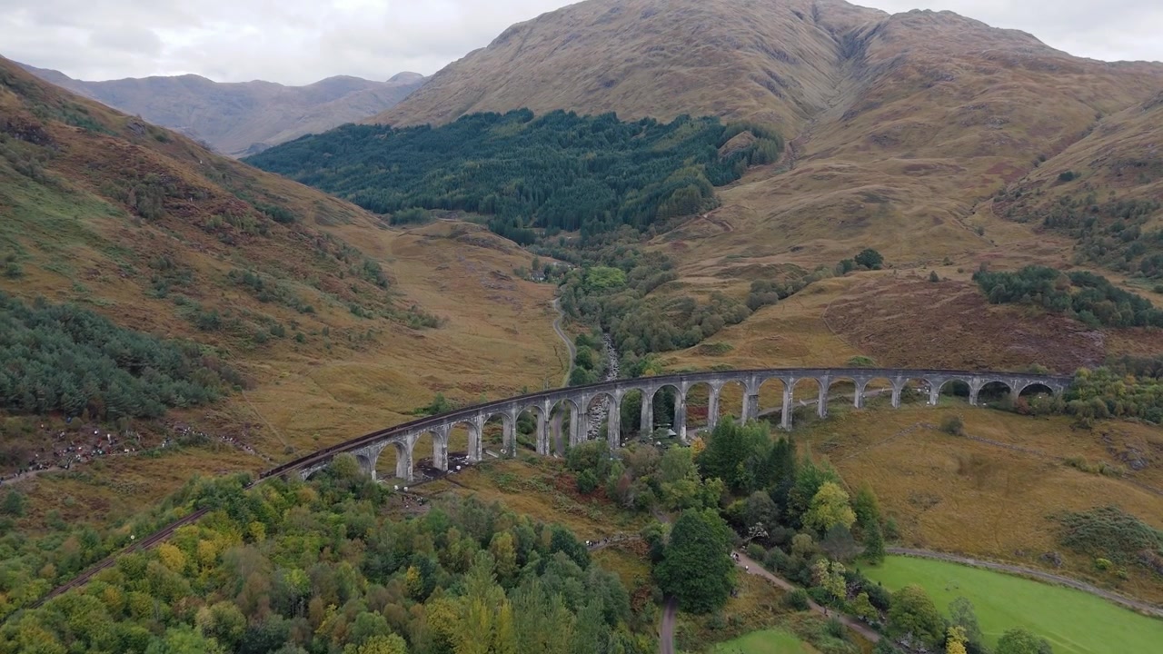 Aproximación rápida al viaducto de Glenfinnan, Escocia, revelando vistas panorámicas del viaducto y el exuberante paisaje de las Tierras Altas escocesas, vías de tren escénicas cruzando valles verdes