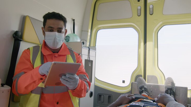 Male Paramedic With Face Mask Using Tablet Computer While Riding In An Ambulance 1
