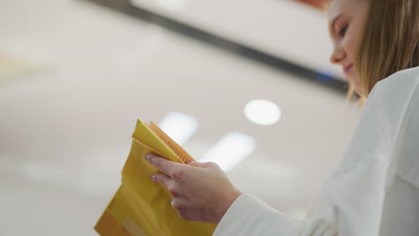 primer plano de manos delicadamente sosteniendo y leyendo un libro cubierto de amarillo, con un fondo suavemente borroso de un moderno centro comercial de iluminación interior