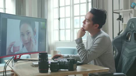 asian cameraman in long sleeved t-shirt thinking while using desktop computer for working at home.