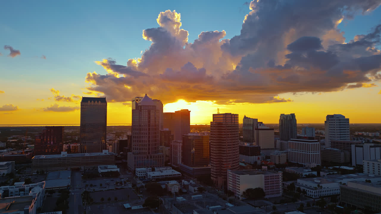 The glowing Tampa skyline during golden sunset with warm clouds, aerial tracking to the left, establishing shot