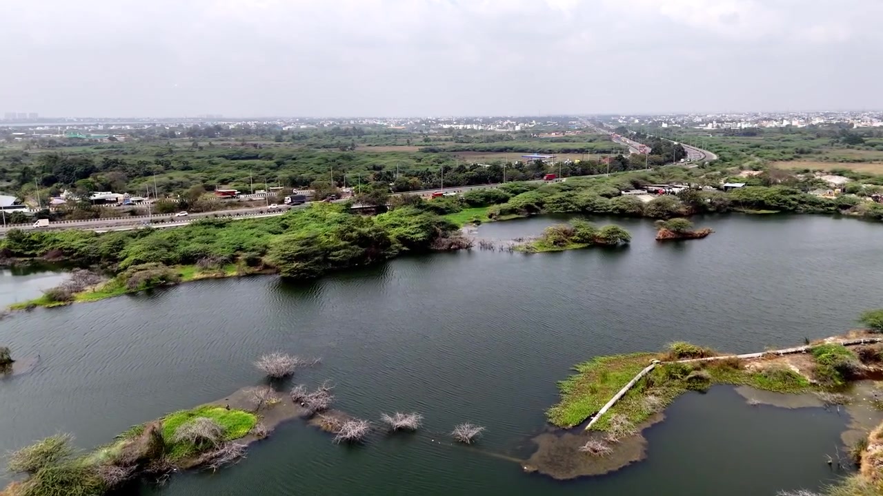 Ripresa con drone che cattura il suggestivo lago di cava a Sikkarayapuram, caratterizzato da impressionanti formazioni rocciose di granito, acqua calma blu-verde e lo skyline in espansione sullo sfondo. Prospettiva aerea.