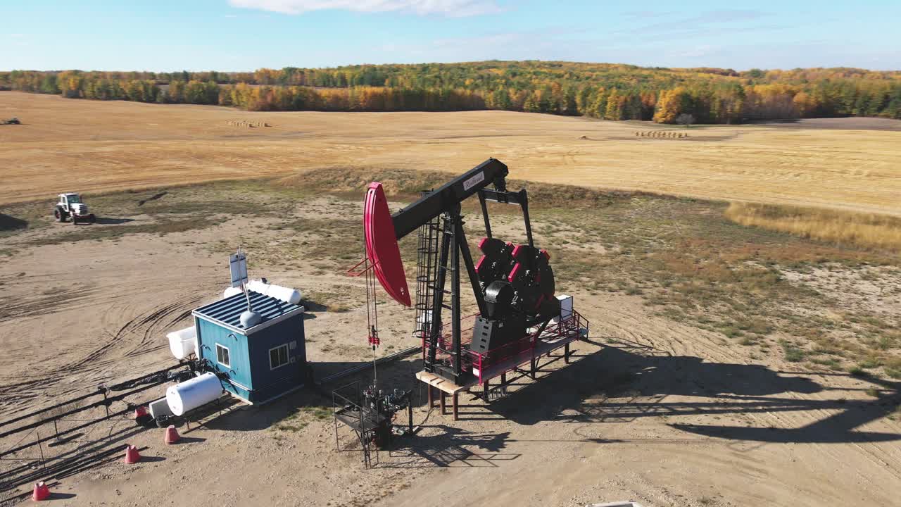 toma aérea de un dron de aceite negro y rojo bomba jack bombeando aceite en un campo en alberta canadá en un día soleado