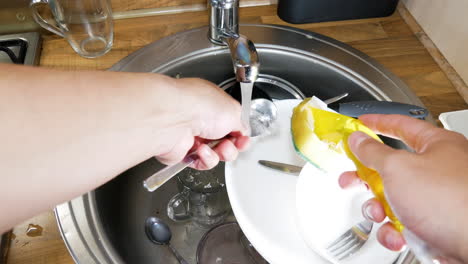 hands of person washing full sink of dirty dishes, pov view