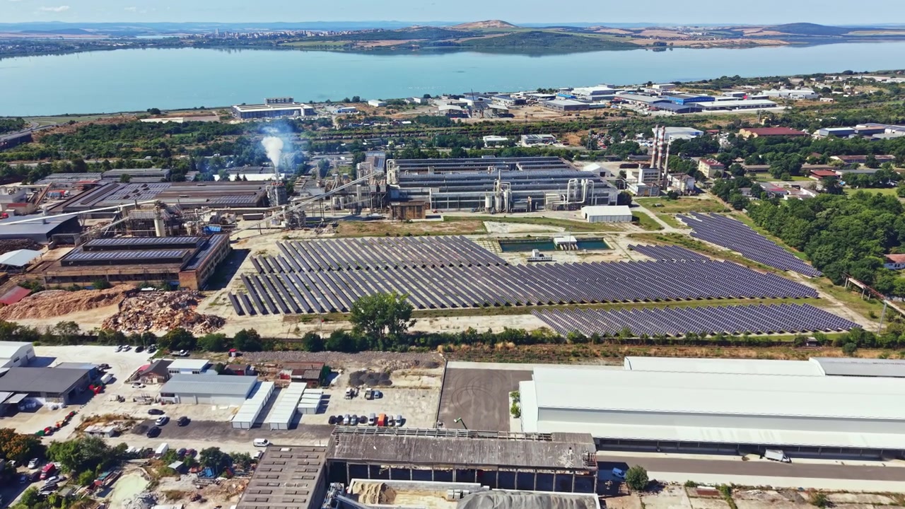 Factory complex with solar panels and water body in the background during daylight