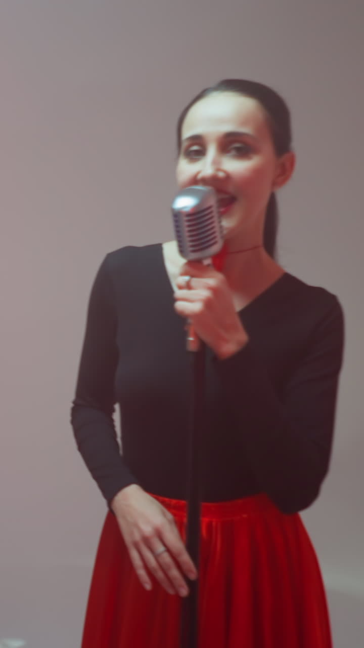 Keyboardist in a black outfit playing a red sampler, a vocalist in a black and red gown singing, and a guitarist playing a red guitar against a grey background