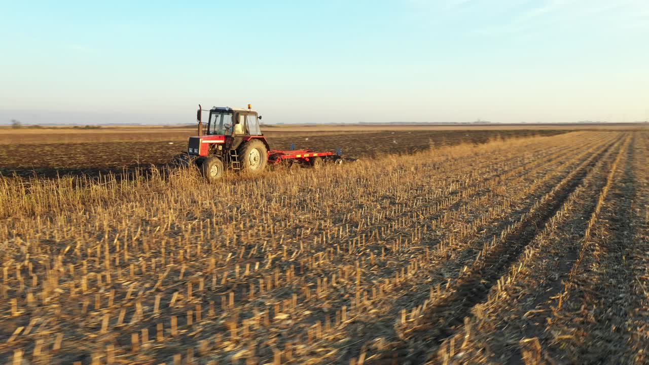 Aerial lateral traveling view of tractor as dragging a disc harrow over agricultural field, farmland