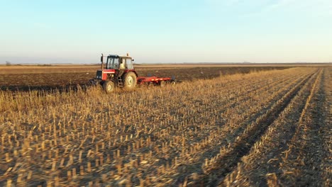 vista lateral aérea de un tractor que arrastra una harra de disco sobre un campo agrícola, tierras de cultivo