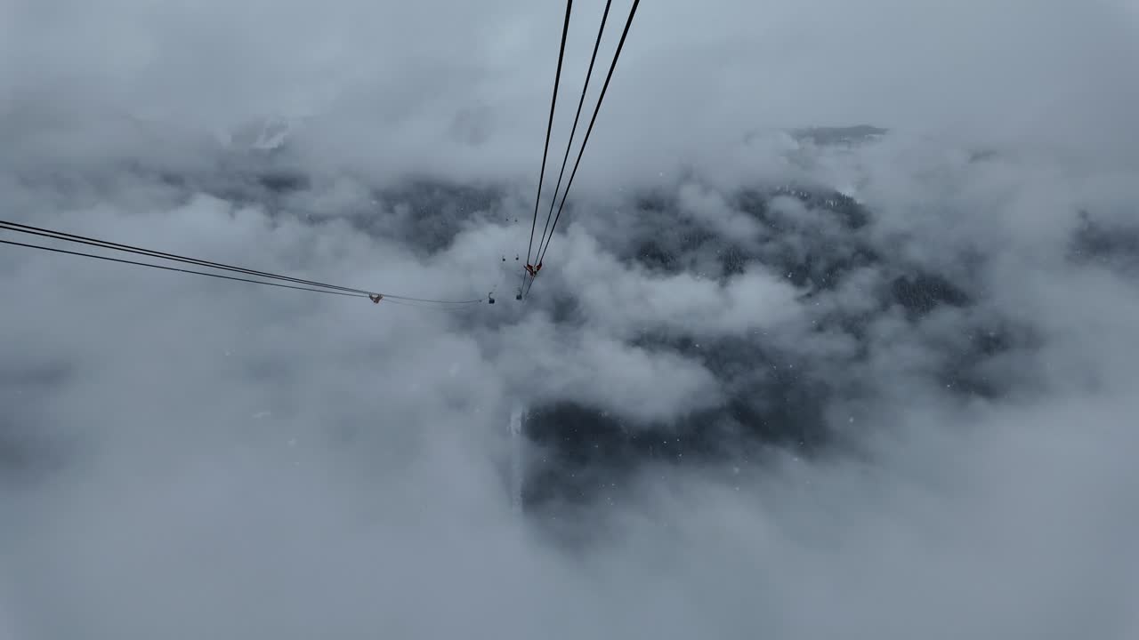 Upp, upp, upp och iväg vid skidorten Whistler Mountain. 4K flygvy från fågelperspektiv som åker med "Peak 2 Peak" trevajersgondolen genom vita, himmelska snömoln