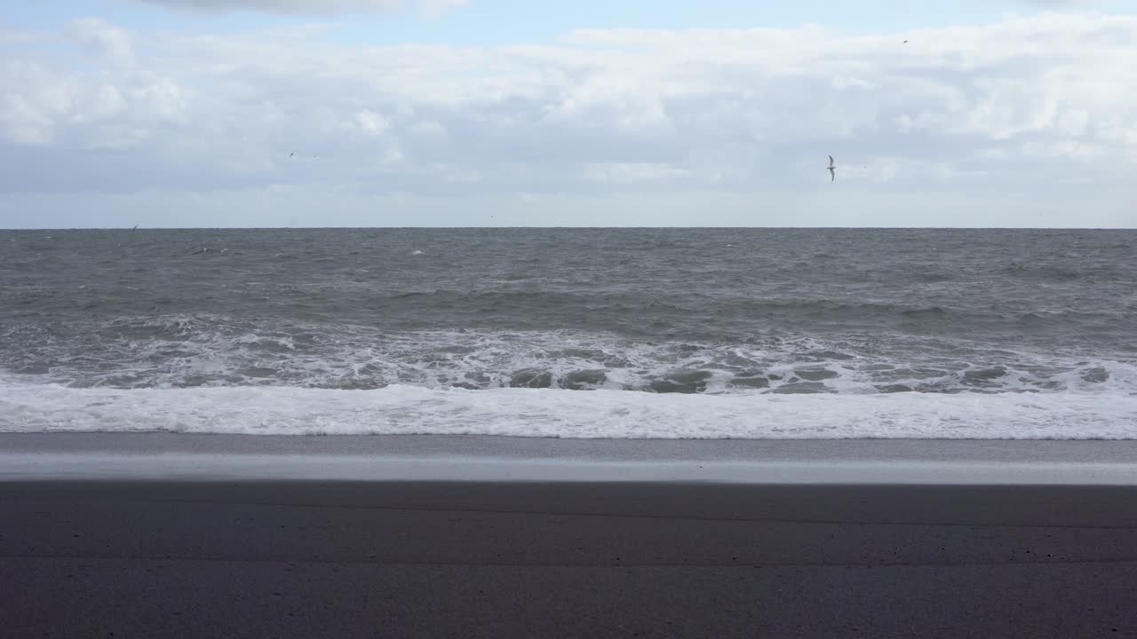 파도가 흐린 하늘 아래 아이슬란드의 검은 모래 해변에 부히고