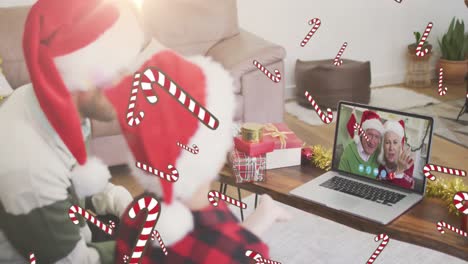 Animation-of-candy-canes,-caucasian-father-and-son-in-santa-hats-on-laptop-video-call-at-christmas