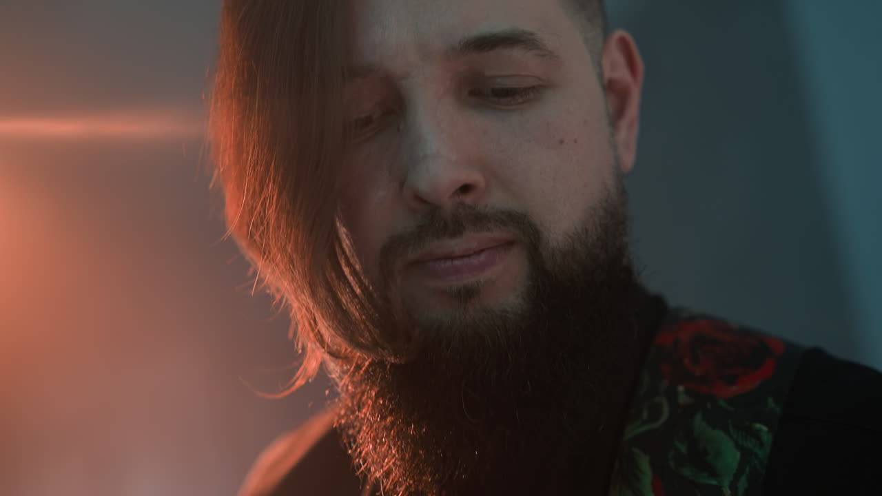 vista de cerca de un hombre barbudo tocando una guitarra contra un telón de fondo con iluminación roja y azul. el guitarrista tiene una expresión intensa, con los ojos cerrados