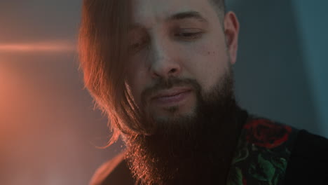 nahaufnahme eines bärtigen mannes, der gegen einen hintergrund mit rotem und blauem licht gitarre spielt. der gitarrist hat einen intensiven ausdruck, mit geschlossenen augen