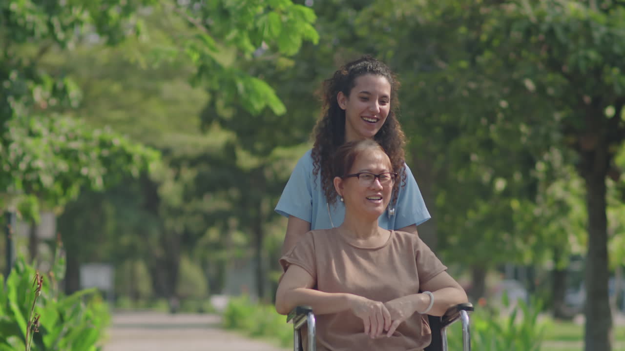 Elderly Caregiver Pushing Senior Woman in Wheelchair Through Park