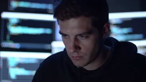 a focused individual engaged in coding or hacking activities with multiple screens displaying complex code lines in a dimly lit environment