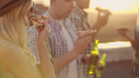 A-female-eat-piece-of-hot-pizza-and-drink-beer-from-a-green-glass-bottle-on-the-party-with-his-fried-in-hot-summer-day.