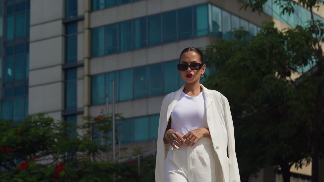 A latina female donning a professional outfit striding through the urban landscape with towering skyscrapers as the backdrop