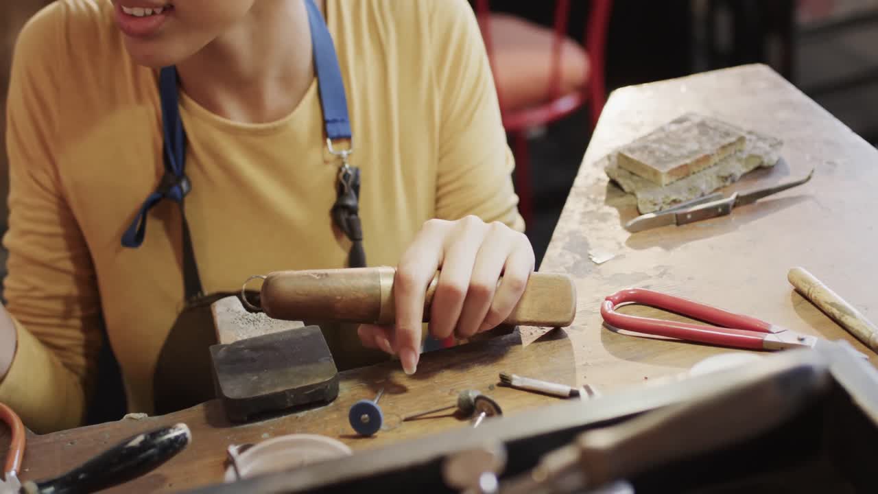 feliz trabajadora biracial en la mesa formando un anillo con herramientas de artesanía en el estudio en cámara lenta