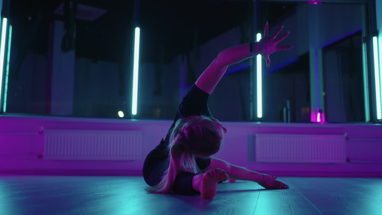 una donna sta facendo esercizi di stretching in una sala fitness seduta sul pavimento e appoggiando il corpo di lato