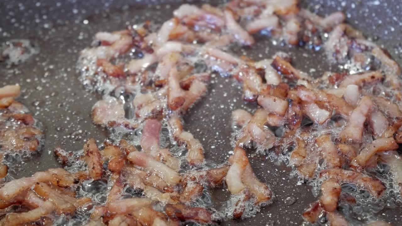 Bacon sizzling in a hot pan, showing crispy pieces frying and bubbling in the oil