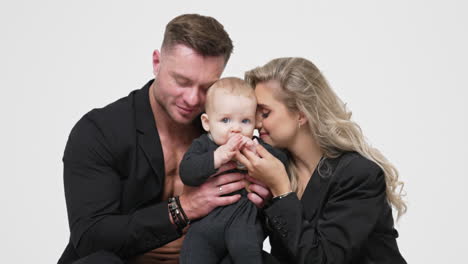 loving and caring family of three with an infant child. beautiful parents kiss and caress their beloved baby. white backdrop.