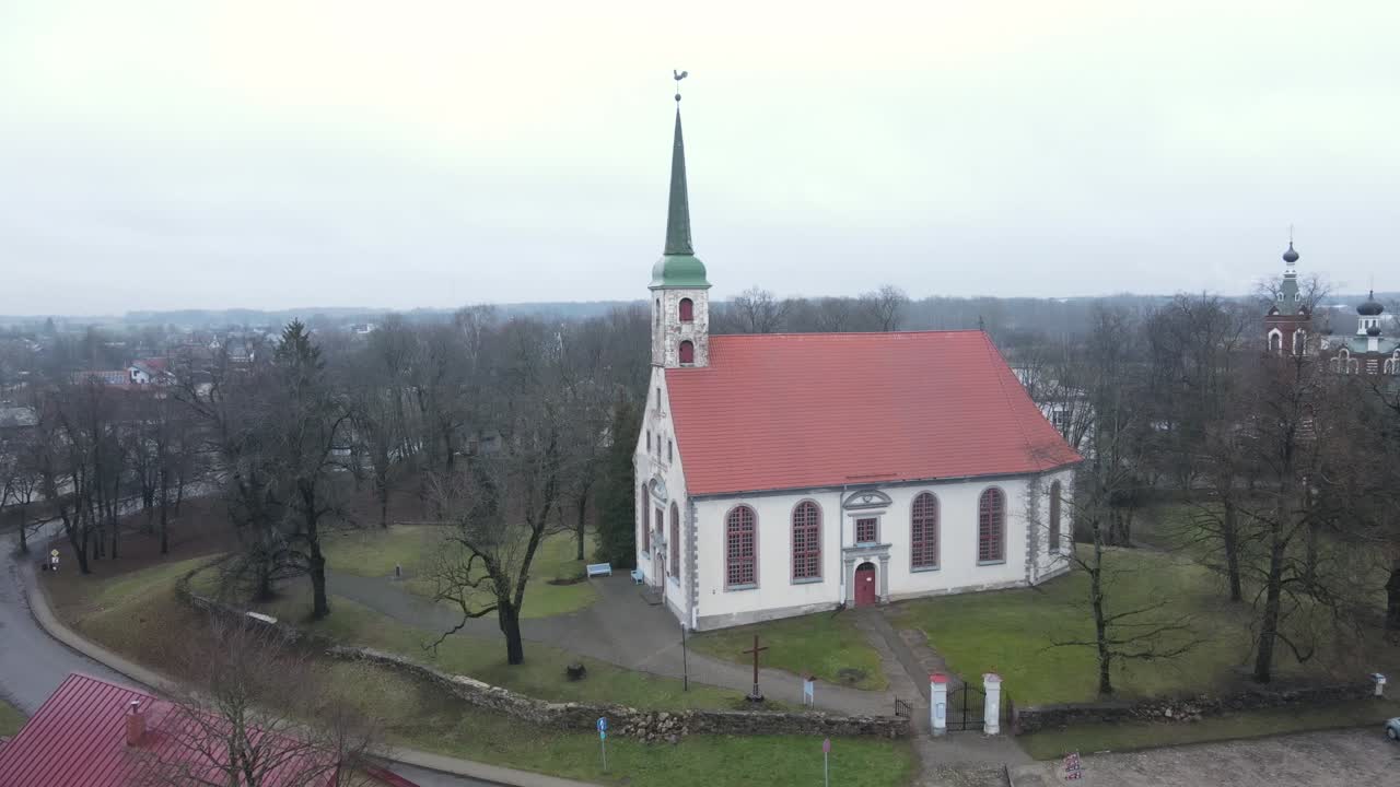 Aerial perspective of Limbazi city showcasing colorful rooftops, historical buildings, a church, and surrounding greenery. A serene, small-town charm is evident in this view.