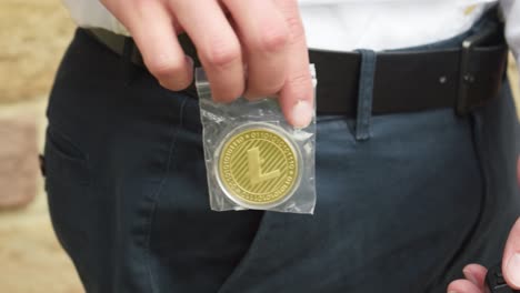 professional businessman pulling out a golden litecoin in a plastic bag out of his pocket. slow motion close up shot.