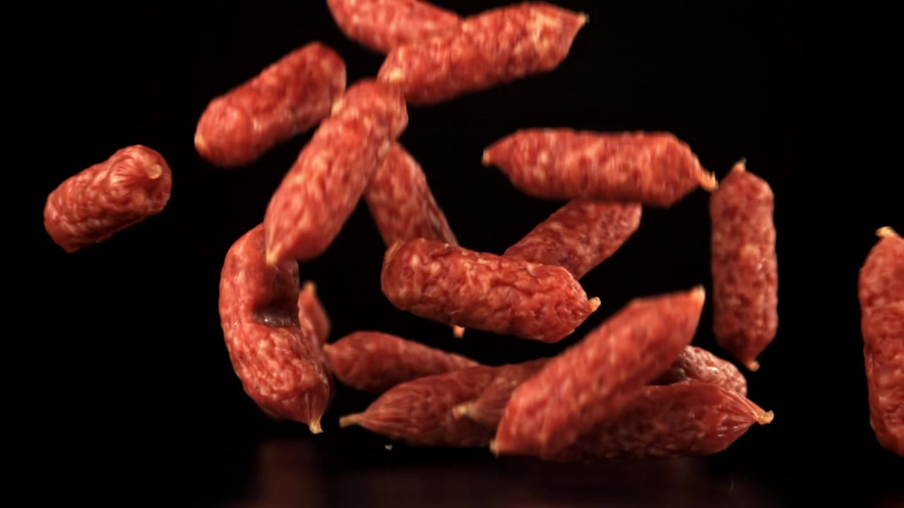 Mini salsicce di salame che cadono al rallentatore su sfondo nero.
