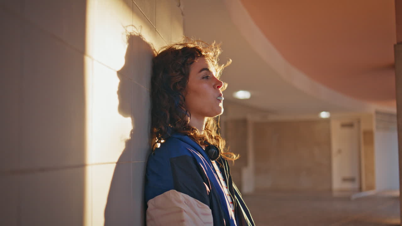 niña disfrutando de la luz del sol de la noche inclinándose hacia el edificio de cerca. mujer soplando burbuja de chicle