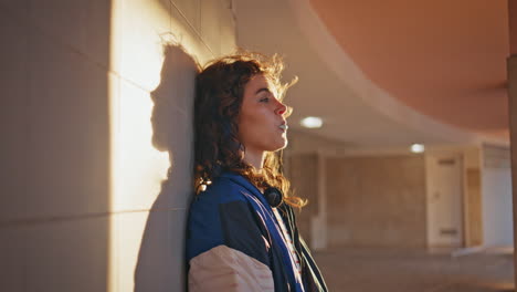 niña disfrutando de la luz del sol de la noche inclinándose hacia el edificio de cerca. mujer soplando burbuja de chicle