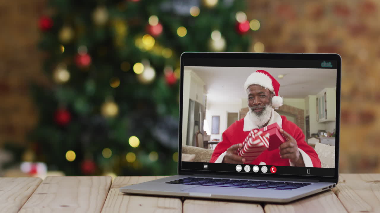 hombre afroamericano senior en disfraz de santa en videollamada en computadora portátil, con árbol de navidad