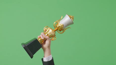 close up of business man's hand holding a gold trophy up in the air to celebrate winning as the first winner on green screen background in the studio