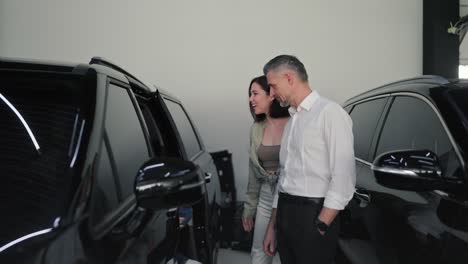 family in a car dealership a little blond boy goes inside a modern black car while his mother and father inspect it while in a car dealership and talk about modern cars