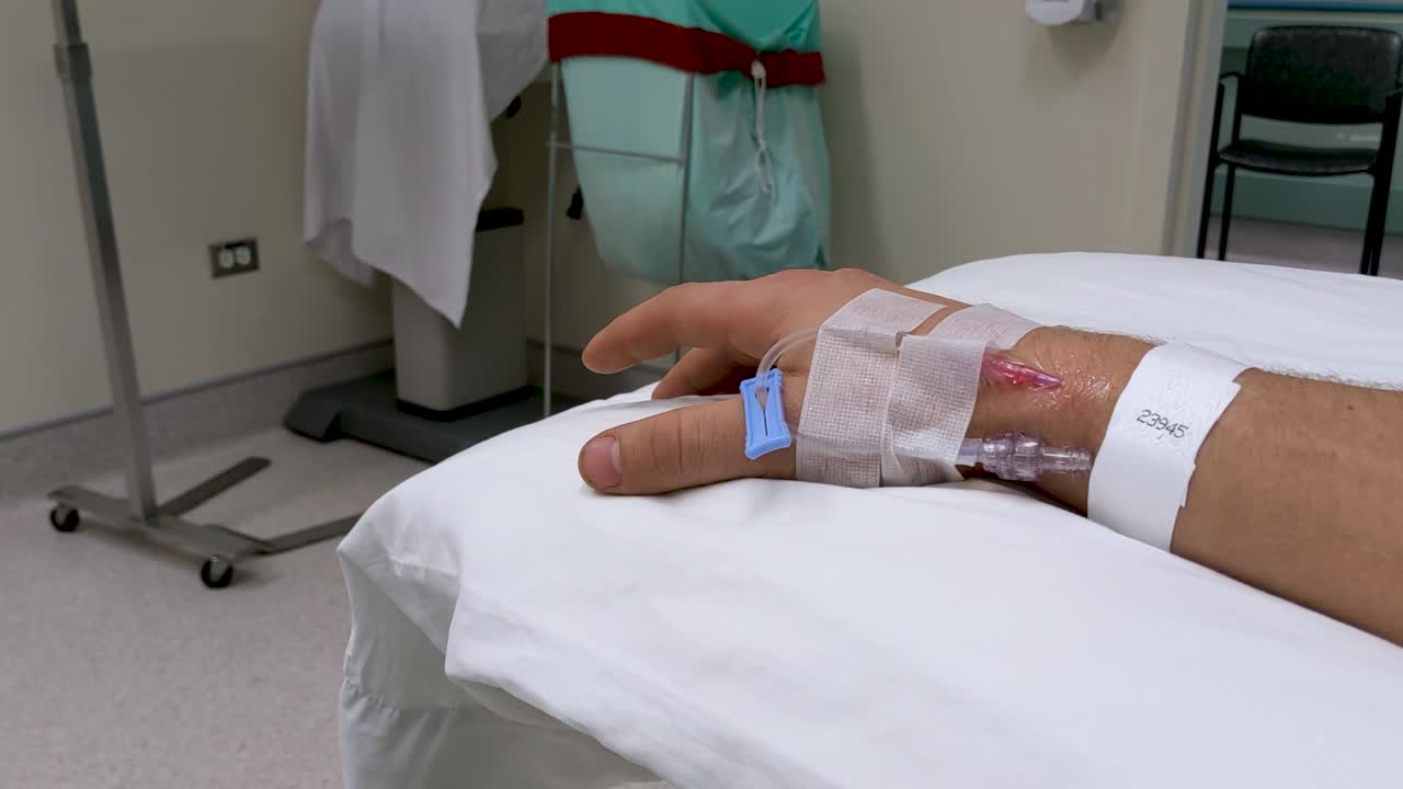 movimientos lentos de la mano de la mano derecha masculina caucásica irreconocible en un escenario médico con iv en la muñeca