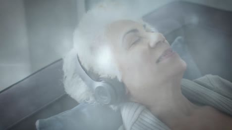 Animation-of-glowing-light-over-happy-senior-woman-listening-to-music-with-headphones