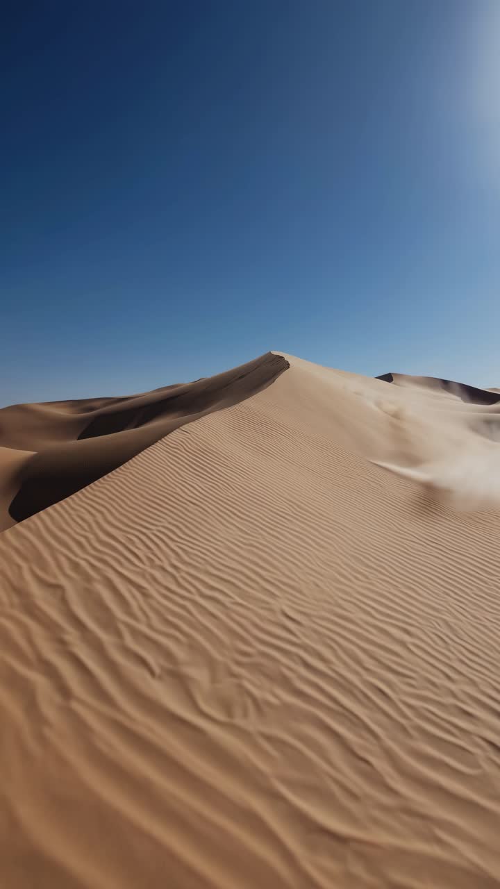 A sweeping low-angle shot of vast desert dunes under a clear blue sky, capturing the serene beauty