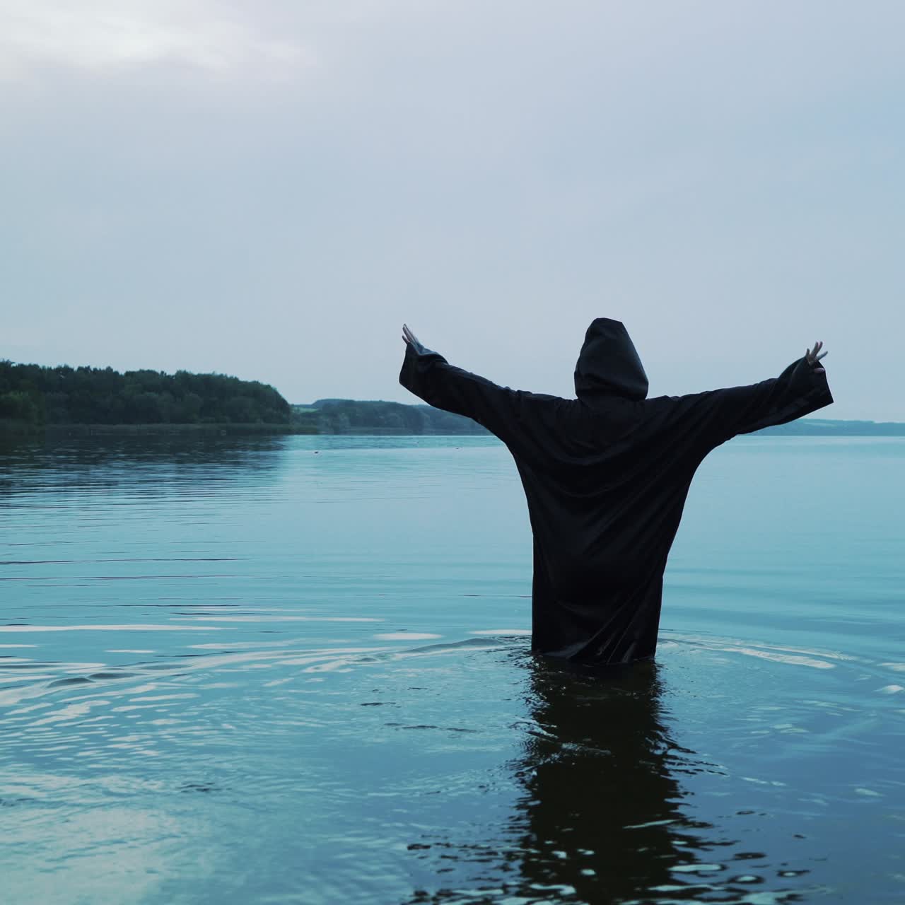 Female figure in a black robe enters the water. Halloween costume