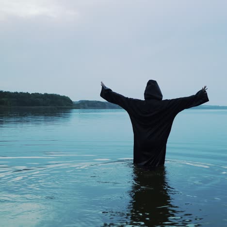 female figure in a black robe enters the water. halloween costume