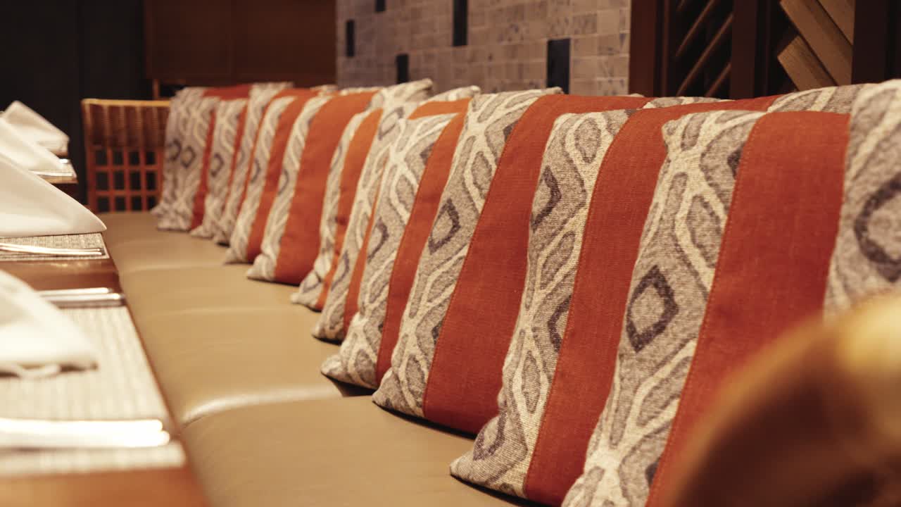 Fila di cuscini decorativi con motivi tribali nei toni del terracotta e del grigio che poggiano su una panca in pelle in uno spazio da pranzo professionale