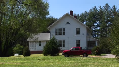 A-Newer-Model-Red-Pickup-Sits-Parked-In-Front-Of-A-Quaint-White-Farmhouse