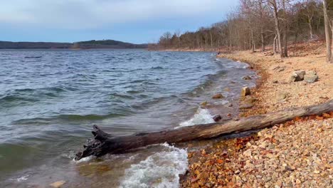 Log-hit-by-waves-on-the-rocky-shoreline,-Table-Rock-Lake-Missouri,-Stationary-Shot