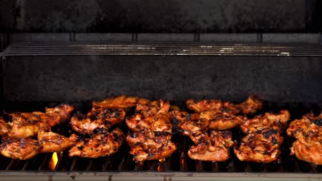 still shot of bbq chicken cooking on a gas grill with the hood open and flames and smoke showing