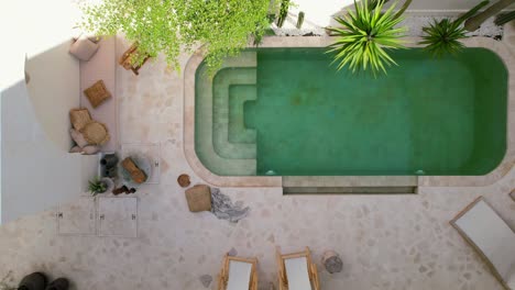 aerial top down slow motion of tropical palms and white furnishing around white pool villa in bali