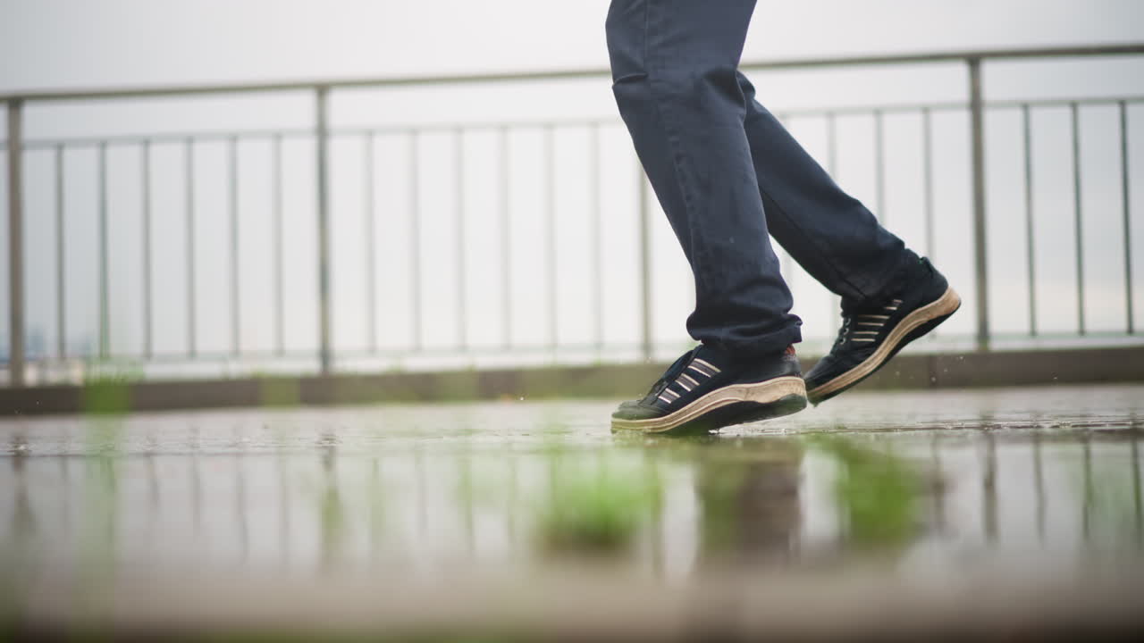carrera rápida por una terraza sobre pavimento mojado con unas zapatillas deportivas levantando gotitas, un corredor decidido atravesando la llovizna junto a una barandilla de metal, la combinación del trayecto matutino y el entrenamiento atlético como mensajero, corredor