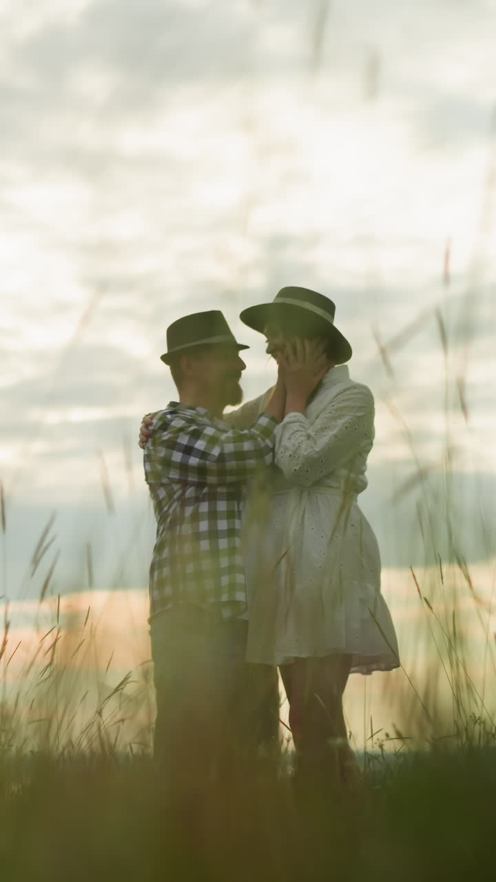 una pareja amorosa se sostiene tiernamente en un campo de hierba, rodeada de un paisaje sereno bajo un cielo nublado. la mujer, en un vestido blanco, y el hombre, en una camisa a cuadros