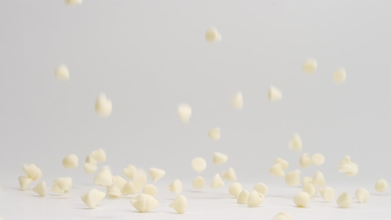 chispas de chocolate blanco cayendo y rebotando sobre una mesa blanca y aterrizando en un montón a cámara lenta