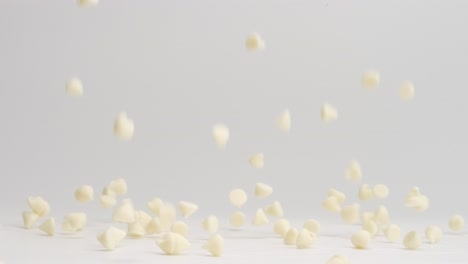 chispas de chocolate blanco cayendo y rebotando sobre una mesa blanca y aterrizando en un montón a cámara lenta