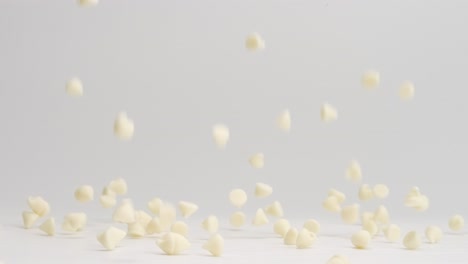 white chocolate chips falling and bouncing around on white table top and landing in a pile in slow motion