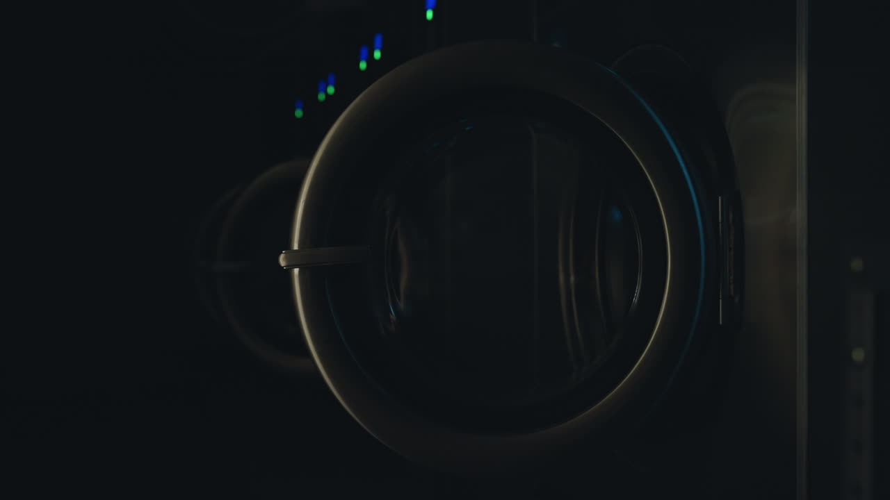 Close up modern washing machine door open inside laundry room as light switches off, stainless steel design emphasizes clean interior space, portraying shutdown moment in cleaning facility