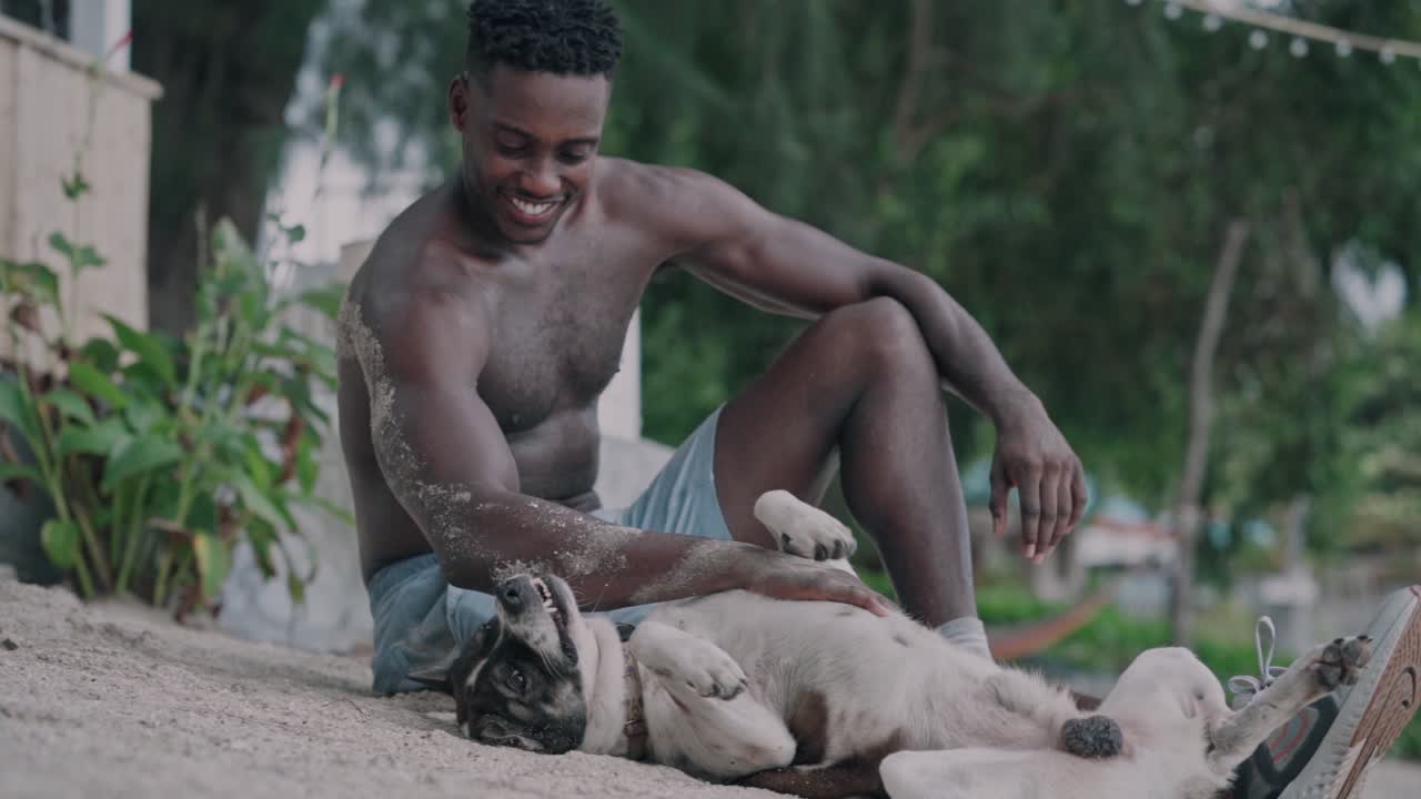 Giovane uomo felice che accarezza cani su una spiaggia sabbiosa